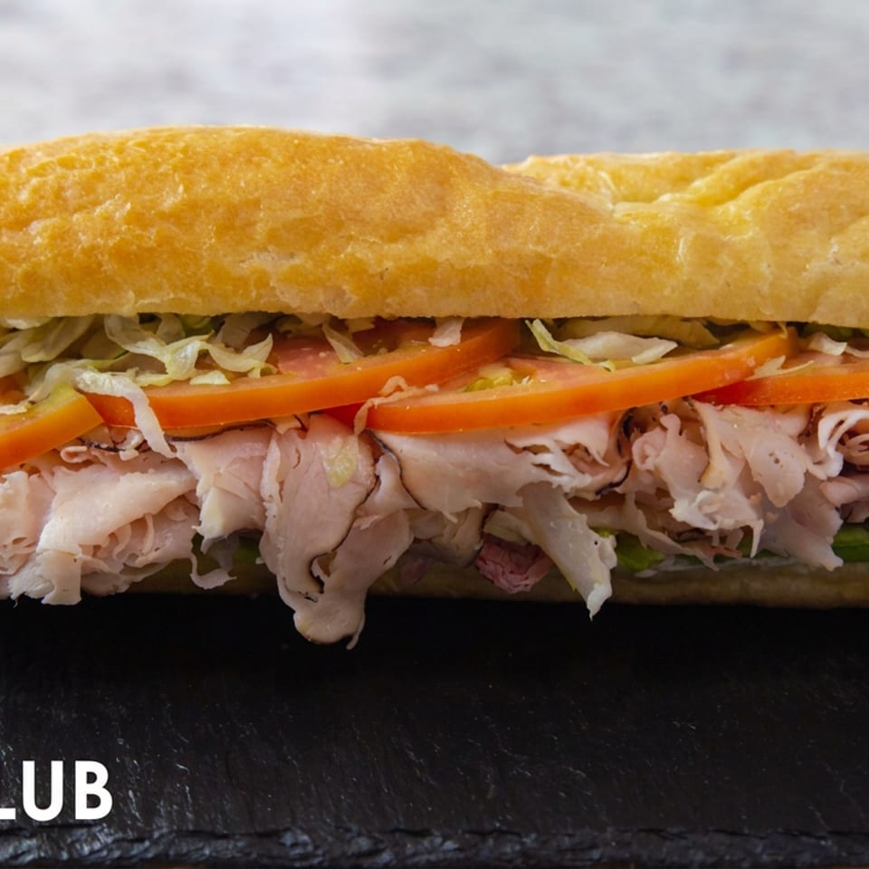 NYC Club sandwich with sliced turkey, tomato, shredded lettuce, and mayonnaise on a toasted roll.