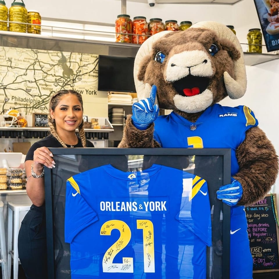 Orleans & York restaurant interior with a woman and ram mascot displaying a signed blue football jersey.