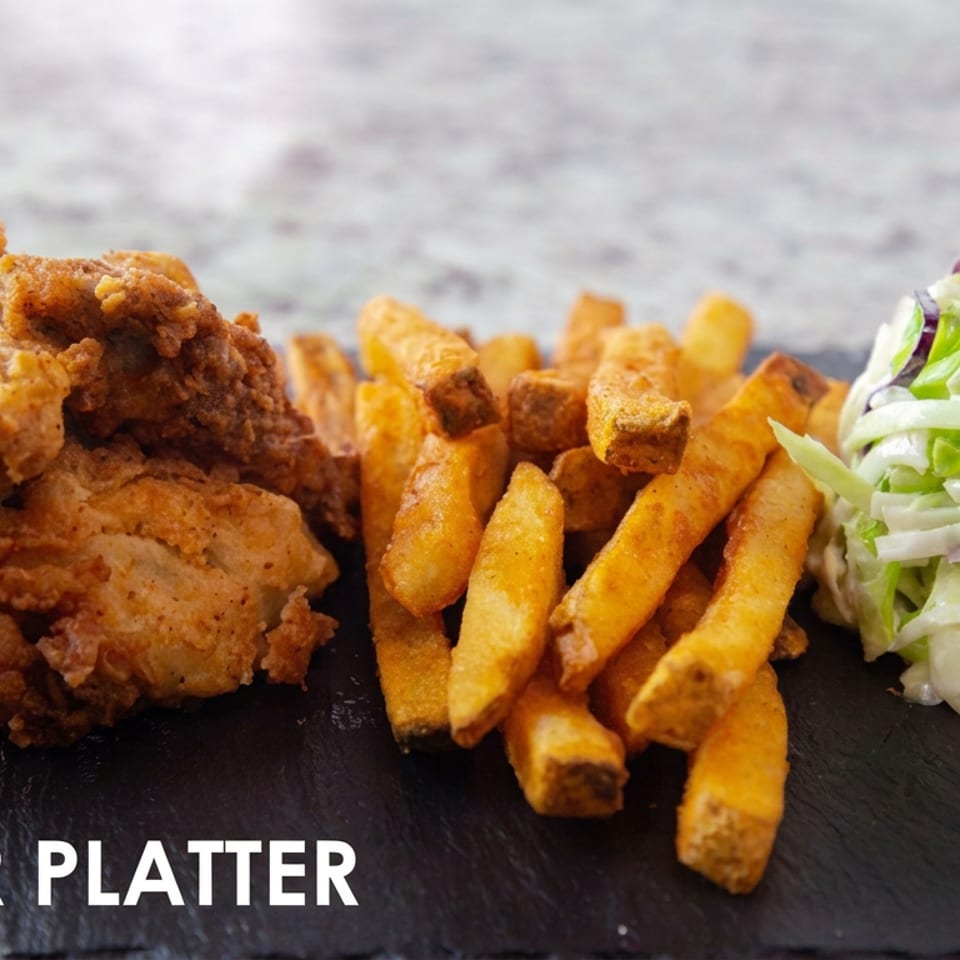 Fried oyster platter with golden fries and creamy cabbage slaw served on a black slate board.