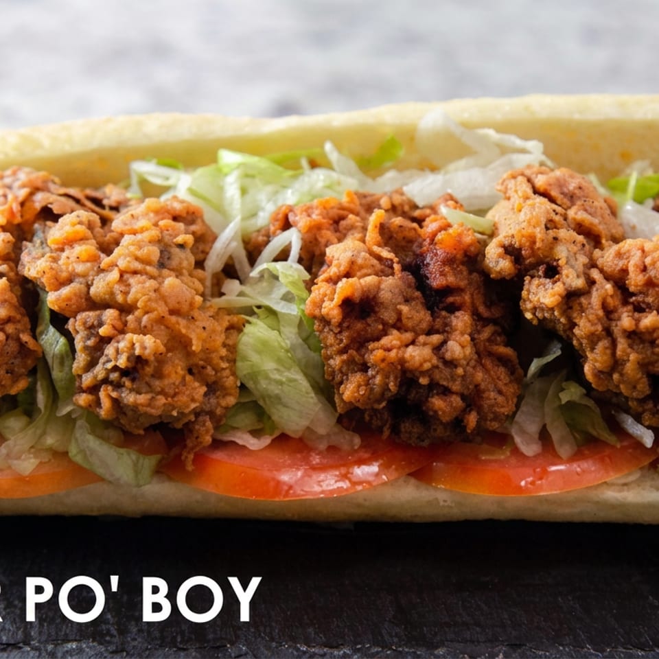 Crispy fried oyster po' boy layered with lettuce and tomato in a soft French bread roll.